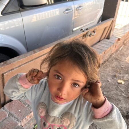 young child smiling at the camera outdoors near a silver vehicle