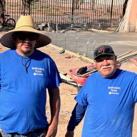 Two men wearing blue t-shirts and hats standing outdoors