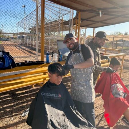 Barbers giving haircuts to young boys outdoors near bleachers
