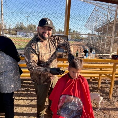 A man in a camouflage jacket cutting a young boy's hair outdoors