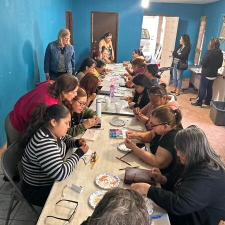 People sitting along a long table doing craft projects inside a room