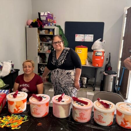 Two women standing behind a table lined with large tubs of ice cream