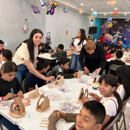 Volunteers assisting children with wooden craft projects in a space-themed room