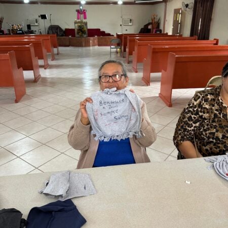 An elderly woman sitting in a church hall holding up a handmade shirt