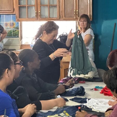 A woman holding up a green fringe top to show a group sitting around a table