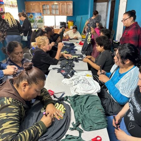 Women sitting along tables cutting, assembling, and working on fabric crafts