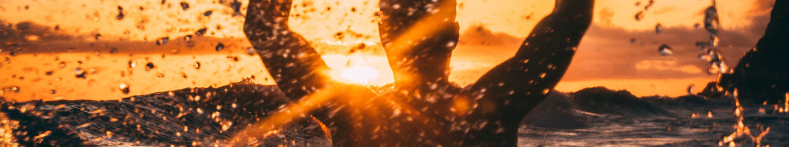 Silhouette of a person with arms raised in ocean water at sunset