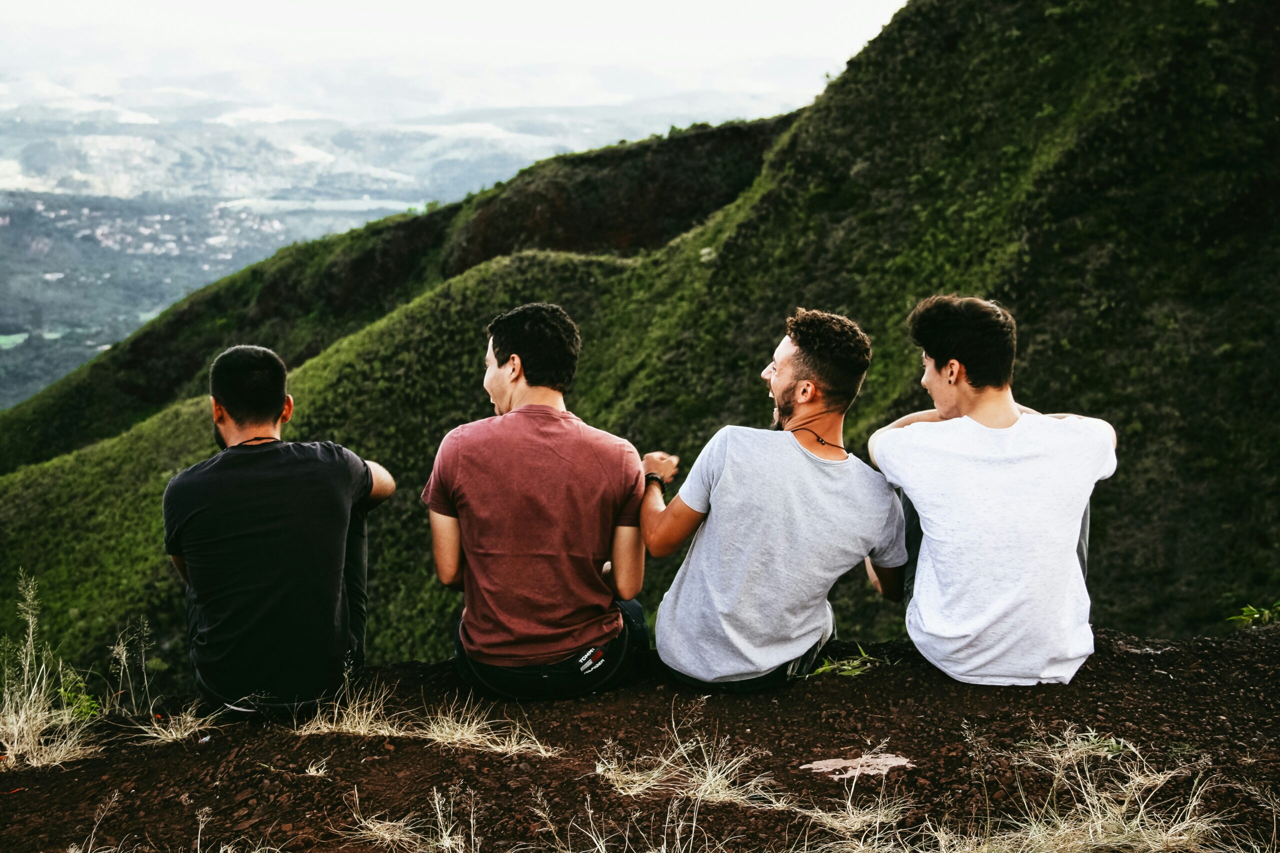 Four young men sitting together on a hillside enjoying a mountain view