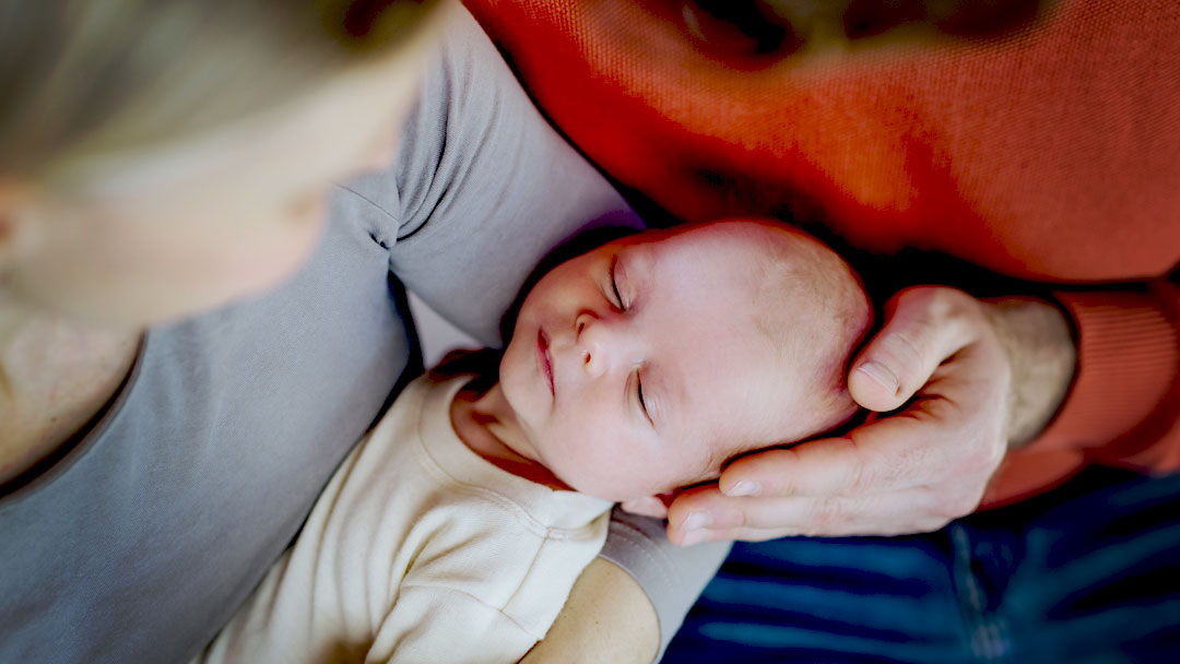 A sleeping newborn baby being gently held by two parents